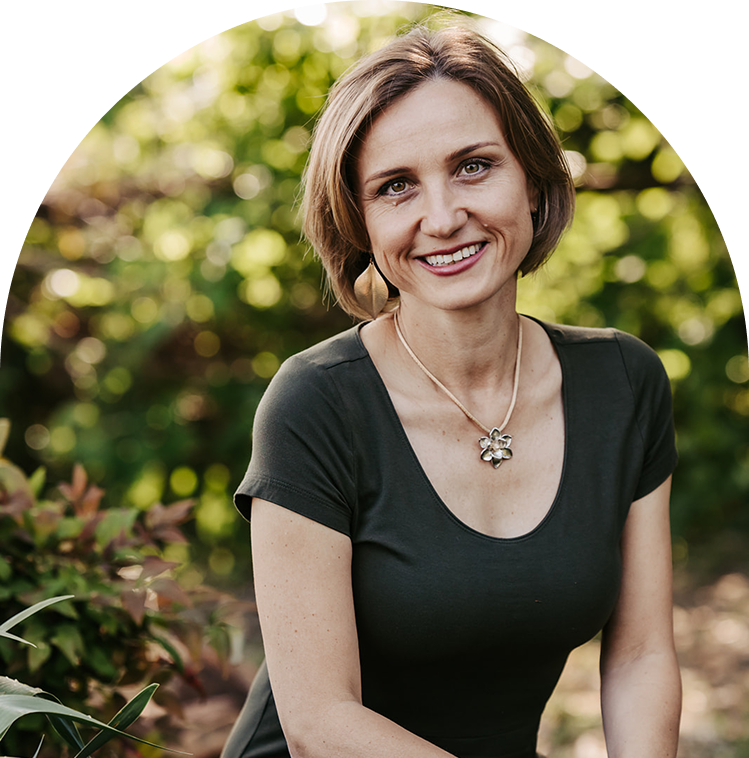 Lana Savit, holistic health coach for women over 40, smiling in a green garden setting wearing a flower pendant necklace.