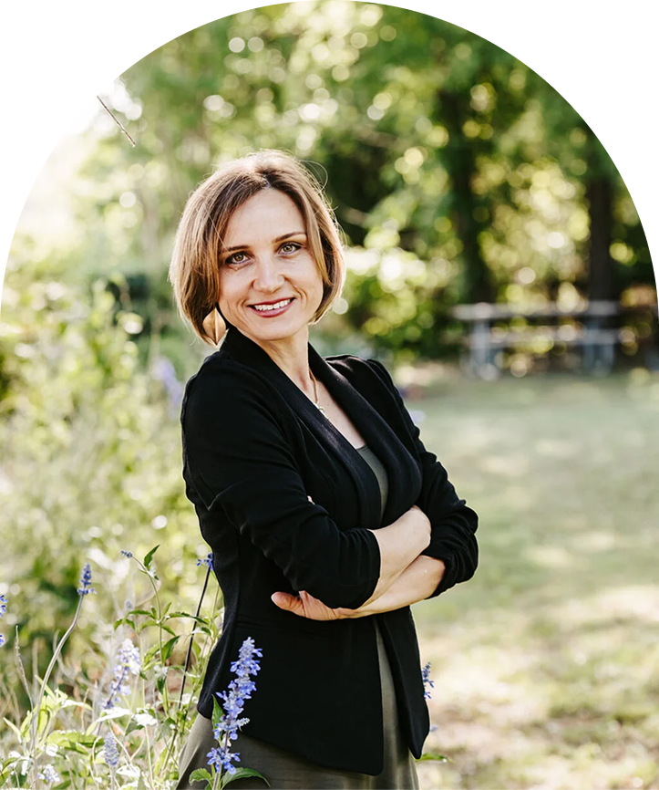 Lana Savit standing confidently in a garden, smiling with arms crossed, wearing a black blazer, symbolizing empowerment, professionalism, and holistic leadership for women over 40.